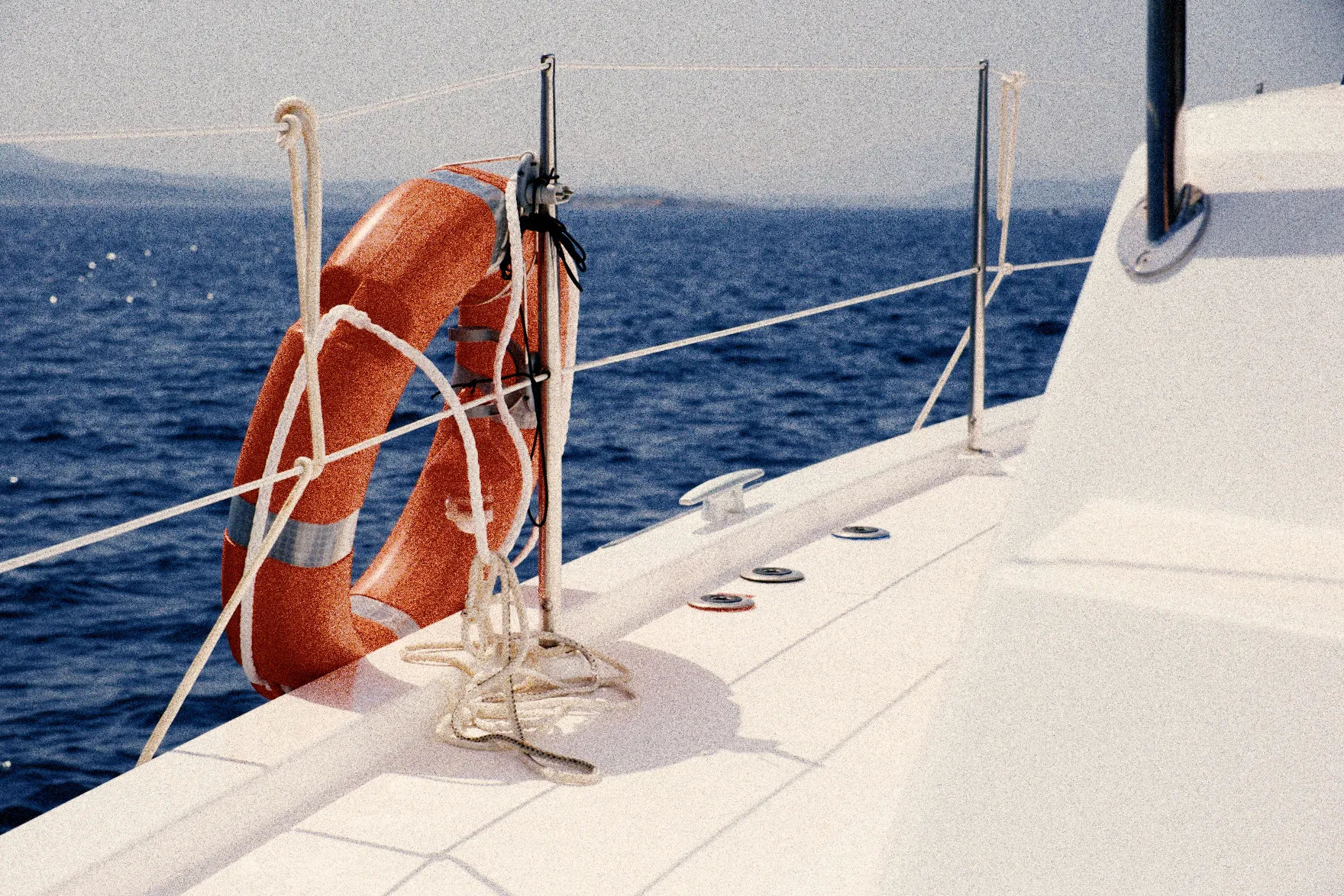 A life ring tied to the rail of a boat, the sea behind it and a white deck in front. The whole frame, with strong grain.