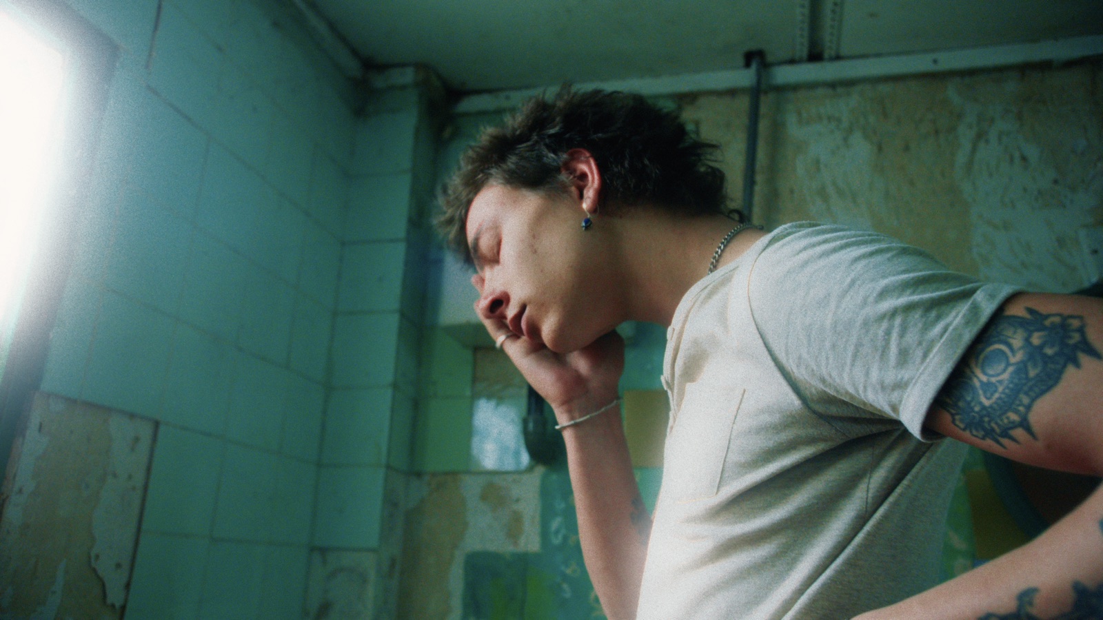 A man leaning on his hand in a green-tiled room, the window light diffused