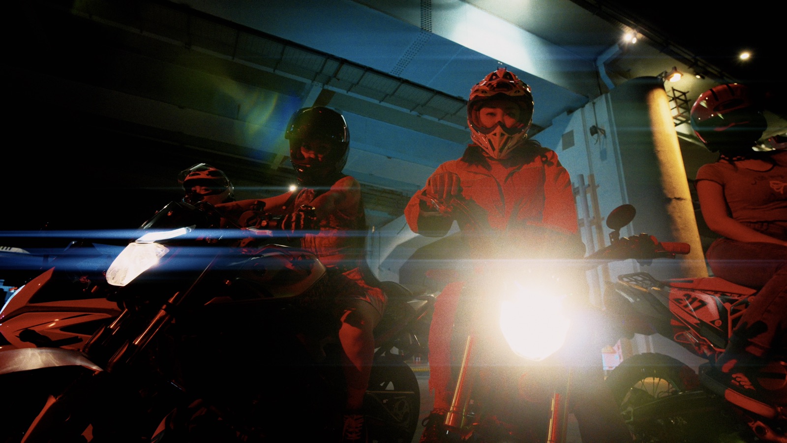 Motorcyclists under a bridge at night, with an anamorphic flare across the headlight