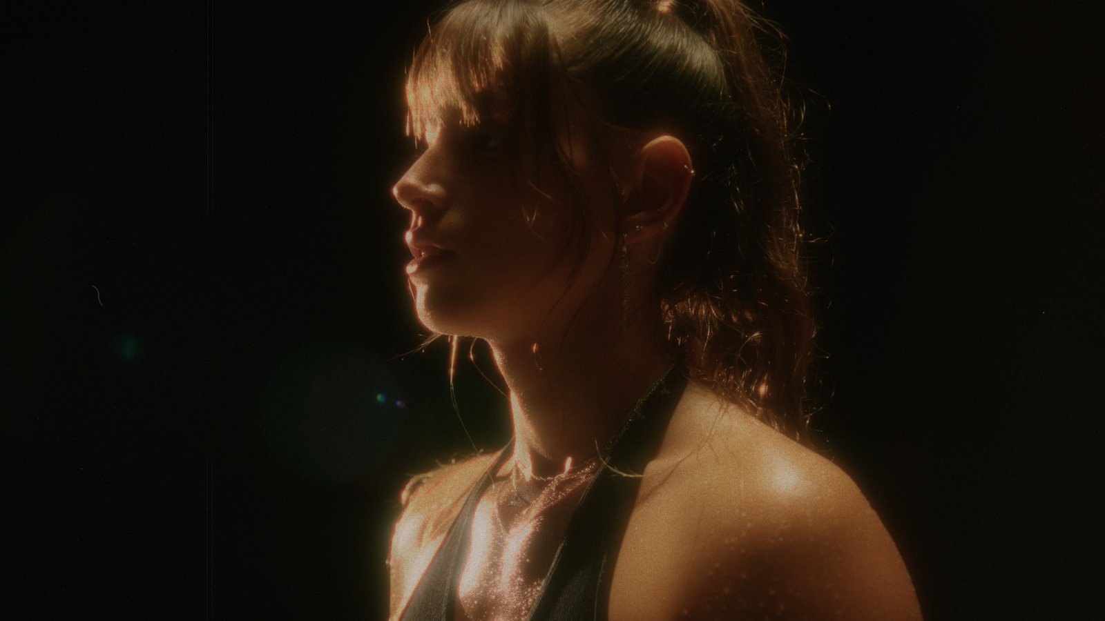 A woman in profile under a single warm light, the light spreading softly through mist
